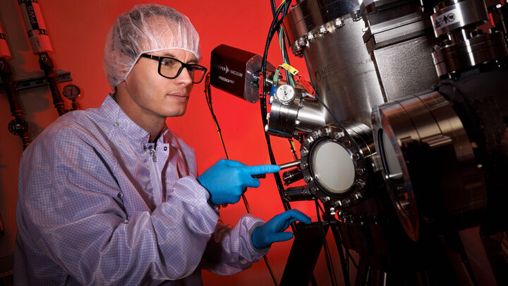 Robert Streubel in protective gear analyzing equipment in a lab with red lighting.