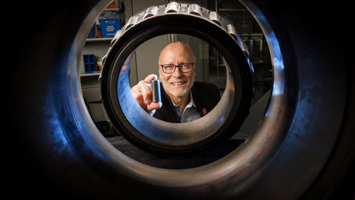 Joe Turner holds a 3D printed railcar bearing. He is photographed through an actual bearing and housing that fits on the end of each axle of a railcar axle.