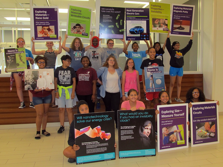 Group of diverse students holding colorful posters about nanotechnology in a bright indoor setting.