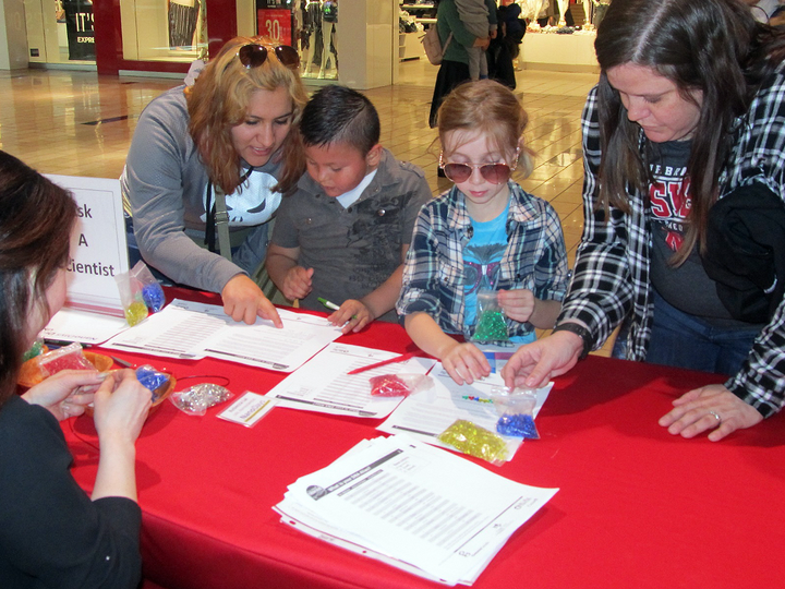 People engaging at a table with educational materials in a mall setting.