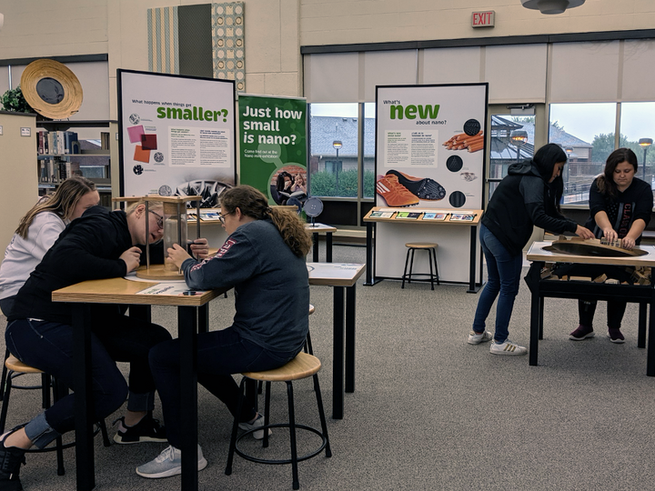 Students engaged at science exhibit tables in a classroom setting.